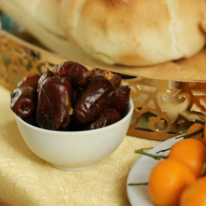 A bowl of dates on an iftar table, with bread and oranges